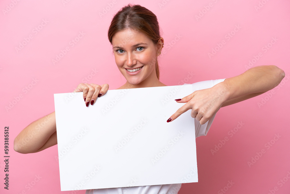 Young caucasian woman isolated on pink background holding an empty placard with happy expression and pointing it Young caucasian woman isolated on pink background holding an empty placard with happy expression and pointing it