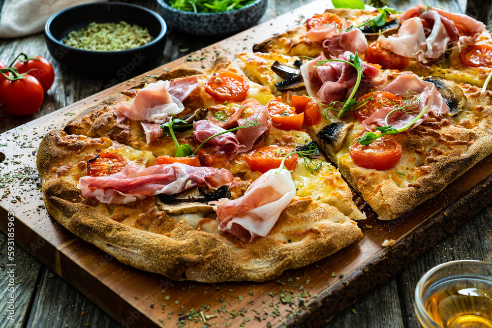 Pinsa Romana with prosciutto crudo , mozzarella and vegetables on wooden table
