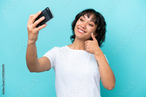 Young Argentinian woman isolated on blue background making a selfie with mobile phone