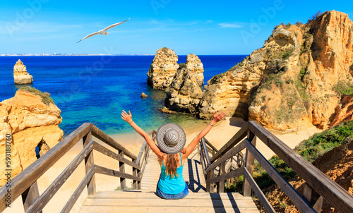 Happy woman tourist sitting on footbridge to beautiful beach praia do camilo,  ponta da piedade- Algarve beach,  tourism in Portugal