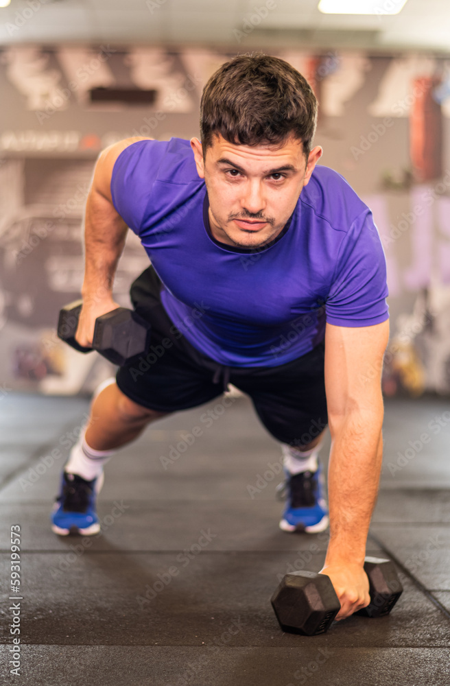 Strong Man Using Dumbbells At Gym
Attractive Man Working Out At The Gym In Plank Position With One Arm Up. He Is Wearing Sports Clothes And Looks Concentrated. 