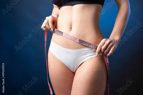 A young slim fit girl with a measuring tape at her waist poses in the studio.