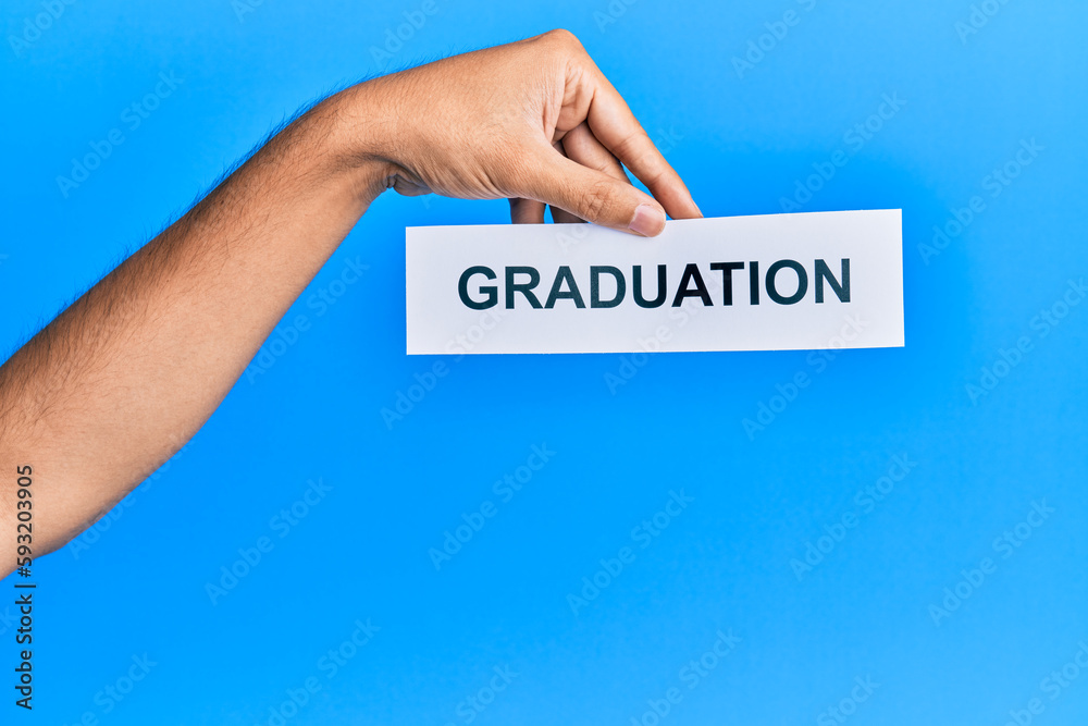 Hand of caucasian man holding paper with graduation word over isolated blue background Hand of caucasian man holding paper with graduation word over isolated blue background