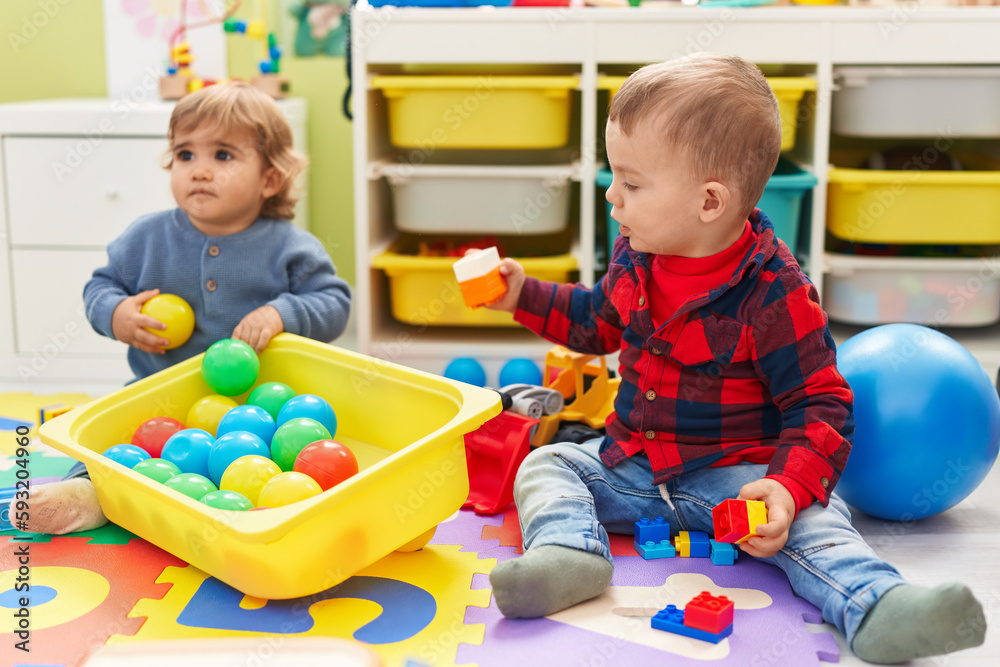 Adorable boys playing with balls and construction blocks sitting on floor at kindergarten Adorable boys playing with balls and construction blocks sitting on floor at kindergarten