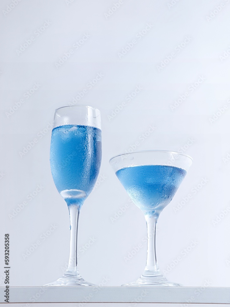 Vertical closeup shot of two glass of blue cocktails on white background.