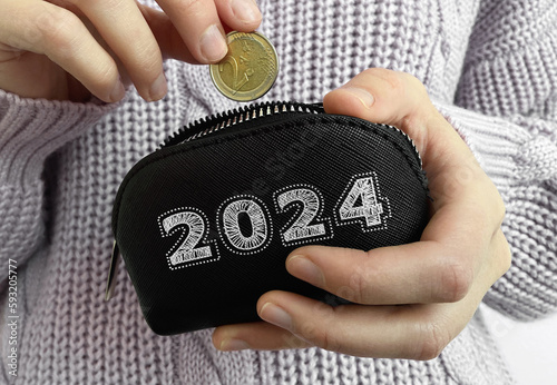 Woman's hand putting coin in black wallet with word 2024