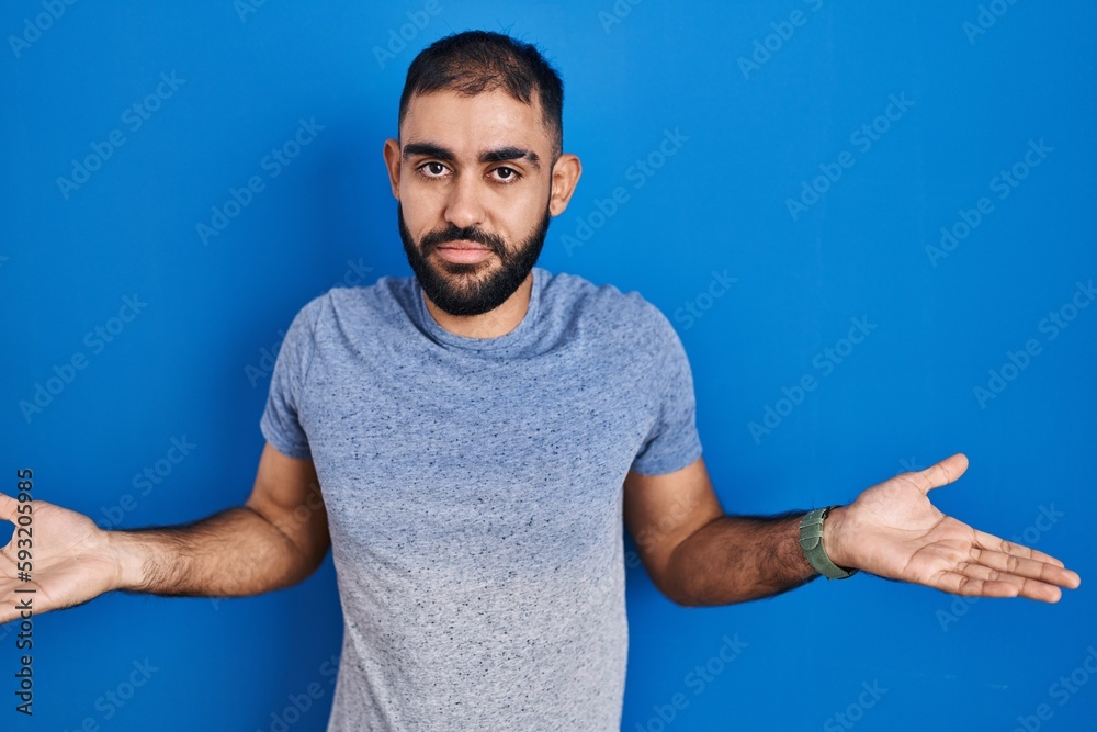 Middle east man with beard standing over blue background clueless and confused with open arms, no idea concept. Middle east man with beard standing over blue background clueless and confused with open arms, no idea concept.