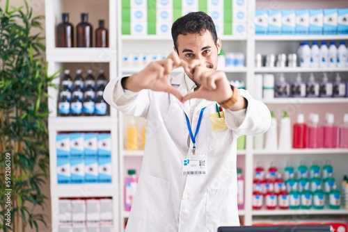 Handsome hispanic man working at pharmacy drugstore smiling in love doing heart symbol shape with hands. romantic concept. © Krakenimages.com