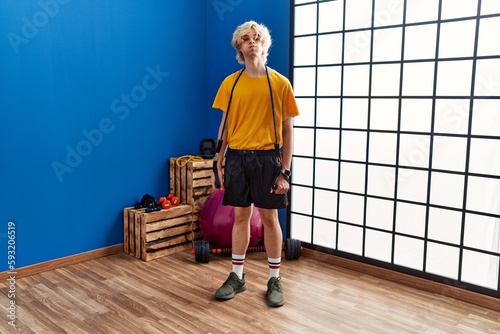 Young man training arm resistance with elastic arm bands puffing cheeks with funny face. mouth inflated with air  catching air.