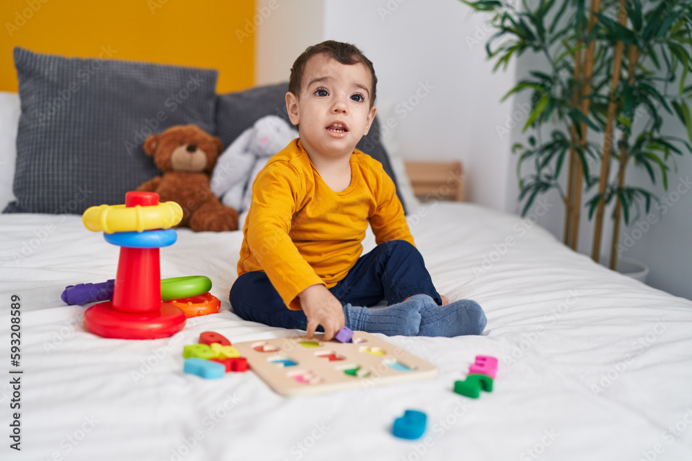Adorable hispanic boy playing with maths puzzle game sitting on bed at bedroom Adorable hispanic boy playing with maths puzzle game sitting on bed at bedroom