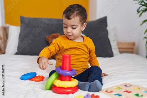 Adorable hispanic boy playing with hoops game sitting on bed at bedroom