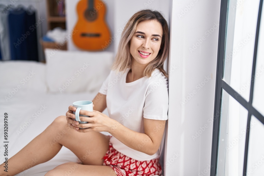 Young woman drinking cup of coffee sitting on bed at bedroom Young woman drinking cup of coffee sitting on bed at bedroom