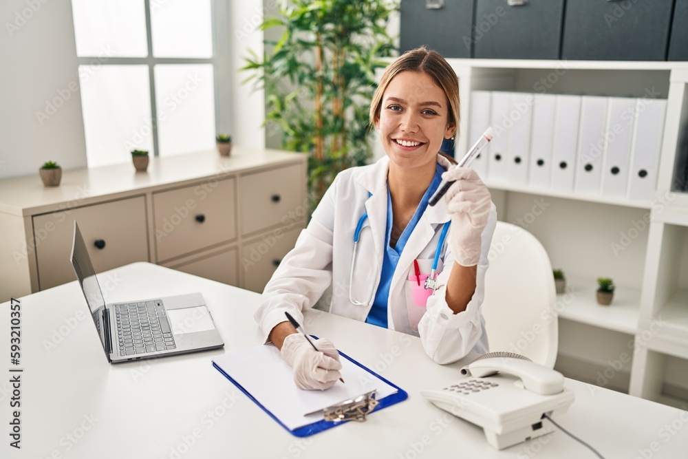 Young hispanic woman wearing doctor uniform analysing blood test tube at clinic Young hispanic woman wearing doctor uniform analysing blood test tube at clinic