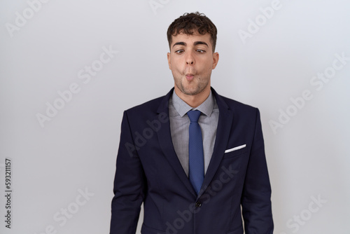 Young hispanic business man wearing suit and tie making fish face with lips, crazy and comical gesture. funny expression.