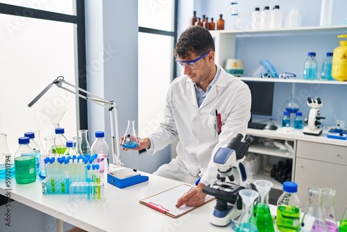 Young hispanic man scientist weighing liquid writing on document at laboratory