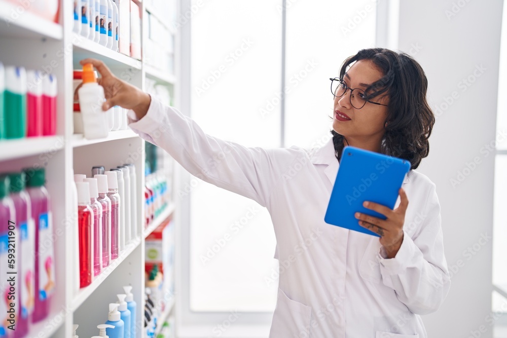 Young beautiful hispanic woman pharmacist using touchpad holding medicine at pharmacy