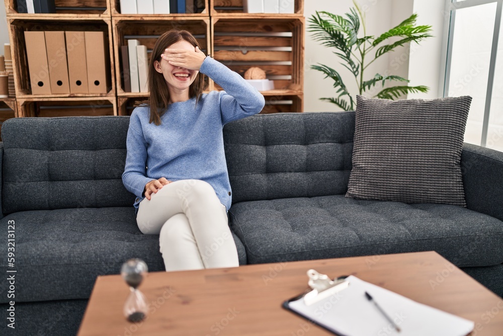 Young brunette woman at consultation office smiling and laughing with hand on face covering eyes for surprise. blind concept.