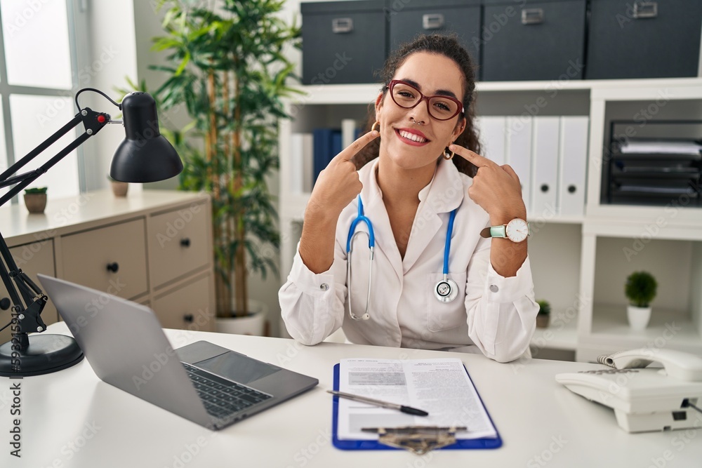 Young hispanic woman wearing doctor uniform and stethoscope smiling cheerful showing and pointing with fingers teeth and mouth. dental health concept. Young hispanic woman wearing doctor uniform and stethoscope smiling cheerful showing and pointing with fingers teeth and mouth. dental health concept.