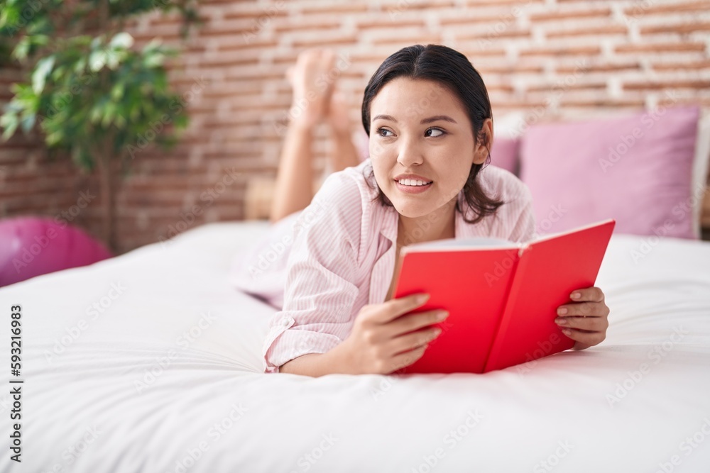 Young hispanic woman reading book lying on bed at bedroom Young hispanic woman reading book lying on bed at bedroom