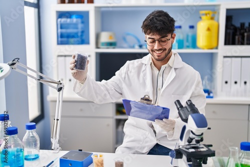Young hispanic man scientist weighing sample reading document at laboratory
