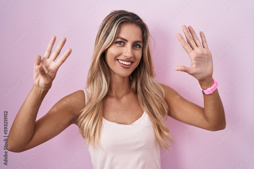 Young blonde woman standing over pink background showing and pointing up with fingers number eight while smiling confident and happy. Young blonde woman standing over pink background showing and pointing up with fingers number eight while smiling confident and happy.