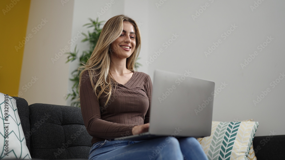 Young blonde woman using laptop sitting on sofa at home Young blonde woman using laptop sitting on sofa at home