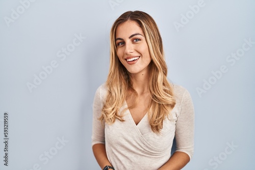 Young blonde woman standing over isolated background with hands together and crossed fingers smiling relaxed and cheerful. success and optimistic