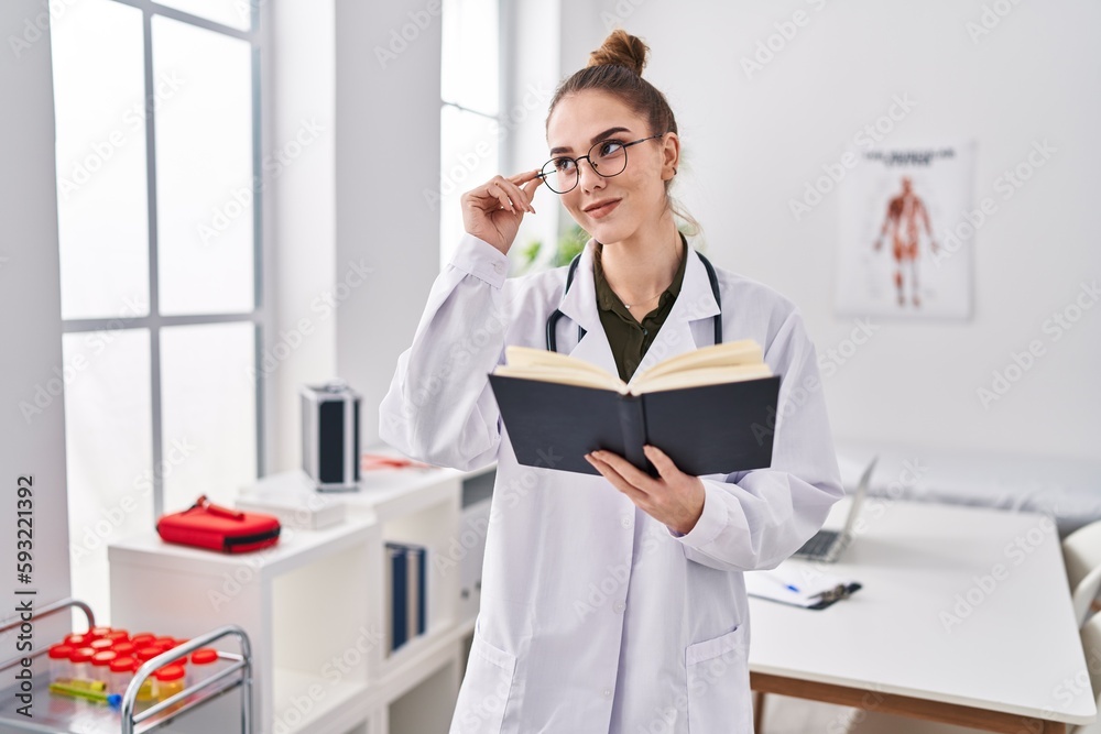 Young woman wearing doctor uniform reading book at clinic