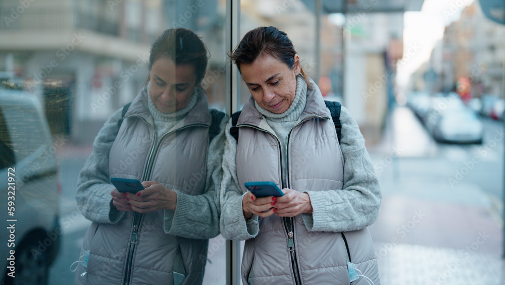 Obraz premium Middle age hispanic woman smiling confident using smartphone at street