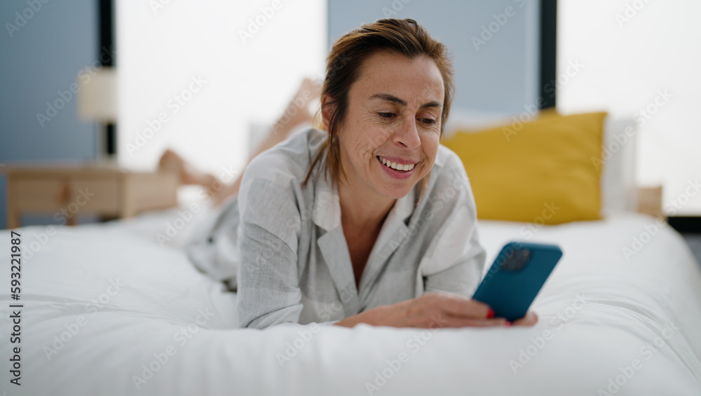 Middle age hispanic woman using smartphone lying on bed at bedroom Middle age hispanic woman using smartphone lying on bed at bedroom