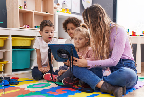 Woman and group of kids having lesson using touchpad at kindergarten photo
