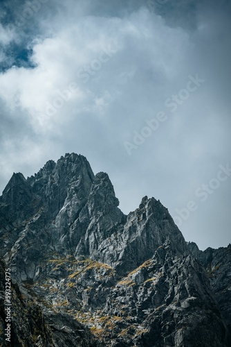 Vertical shot of rocky mountains with a fluffy cloud in the background © Vlad Chețan/Wirestock Creators