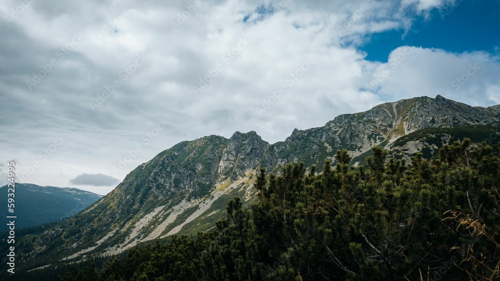 Aerial view of rocky mountains with green vegetation under blue cloudy sky Aerial view of rocky mountains with green vegetation under blue cloudy sky