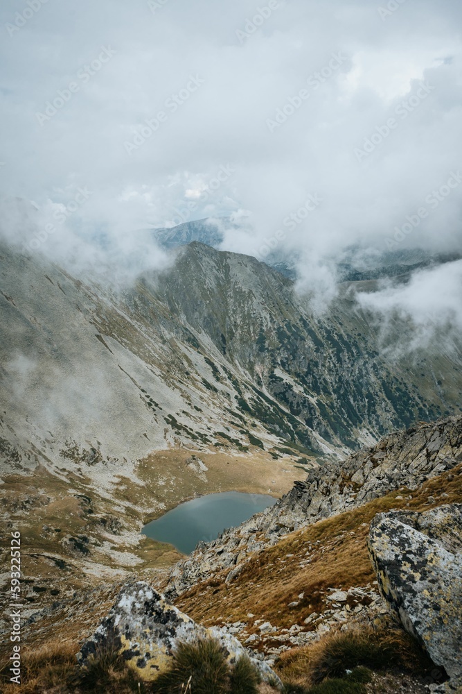 Vertical shot of a rocky mountain landscape with small lake in the middle in fog