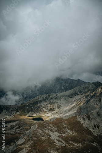 Vertical of a small lake surrounded by the big mountains on a cloudy day during the daytime © Vlad Chețan/Wirestock Creators