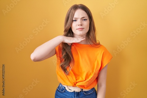 Caucasian woman standing over yellow background cutting throat with hand as knife, threaten aggression with furious violence