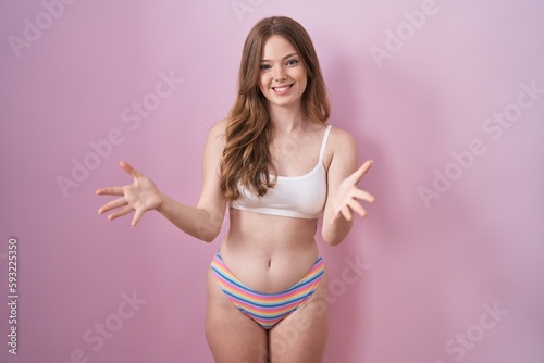 Caucasian woman wearing lingerie over pink background smiling cheerful with open arms as friendly welcome, positive and confident greetings © Krakenimages.com