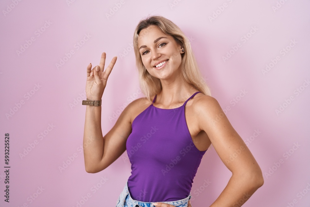 Young blonde woman standing over pink background smiling looking to the camera showing fingers doing victory sign. number two. Young blonde woman standing over pink background smiling looking to the camera showing fingers doing victory sign. number two.