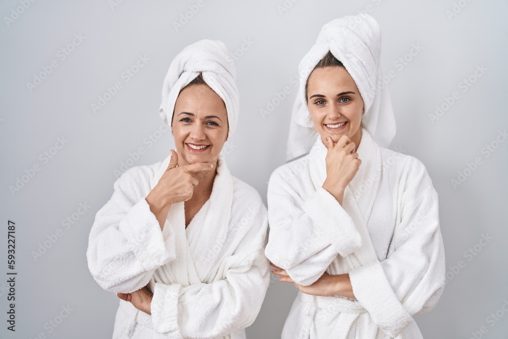 Middle age woman and daughter wearing white bathrobe and towel looking confident at the camera smiling with crossed arms and hand raised on chin. thinking positive. Middle age woman and daughter wearing white bathrobe and towel looking confident at the camera smiling with crossed arms and hand raised on chin. thinking positive.
