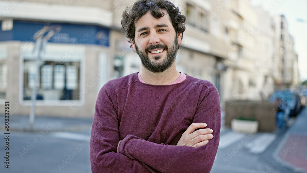 Naklejka premium Young hispanic man smiling confident standing with arms crossed gesture at street