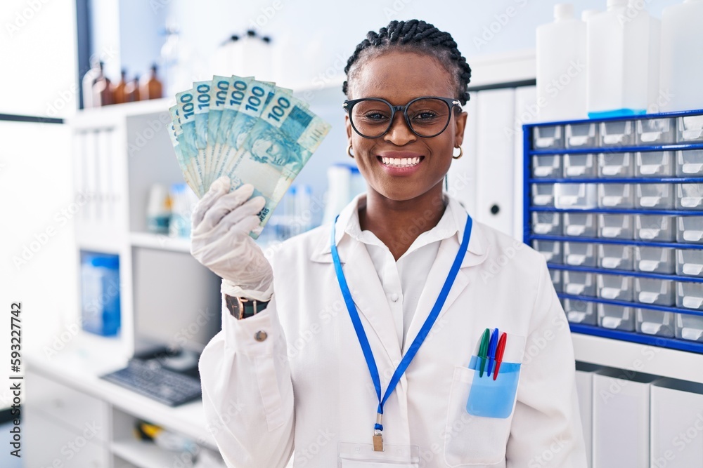 African woman with braids working at scientist laboratory holding money looking positive and happy standing and smiling with a confident smile showing teeth African woman with braids working at scientist laboratory holding money looking positive and happy standing and smiling with a confident smile showing teeth
