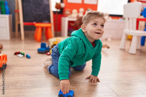 Adorable caucasian boy playing with car toy sitting on floor at kindergarten