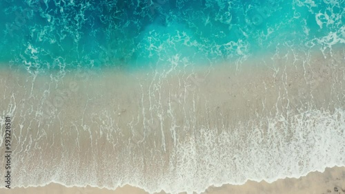 Aerial top view of ocean turquoise blue waves break on a beach. Aerial shot of beach with small stones meeting ocean water and foam. Top view of paradise island. tidal wave floods sandy beach. relax.