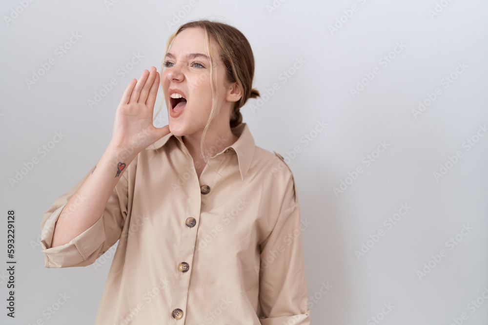 Young caucasian woman wearing casual shirt shouting and screaming loud to side with hand on mouth. communication concept. Young caucasian woman wearing casual shirt shouting and screaming loud to side with hand on mouth. communication concept.