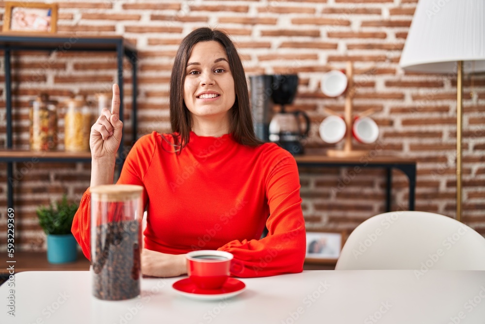 Young hispanic woman drinking coffee at home surprised with an idea or question pointing finger with happy face, number one Young hispanic woman drinking coffee at home surprised with an idea or question pointing finger with happy face, number one