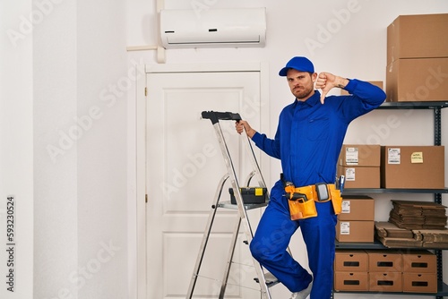 Young hispanic man working at renovation with angry face, negative sign showing dislike with thumbs down, rejection concept