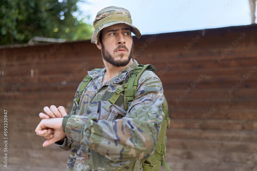 Young hispanic man wearing soldier uniform looking watch at park