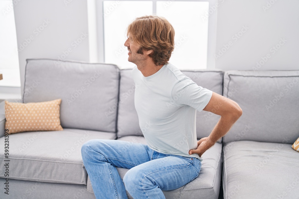 Young man suffering for back ache sitting on sofa at home