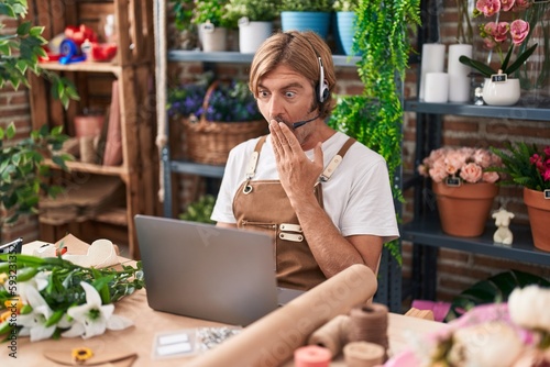 Caucasian man with mustache working at florist shop doing video call covering mouth with hand, shocked and afraid for mistake. surprised expression © Krakenimages.com