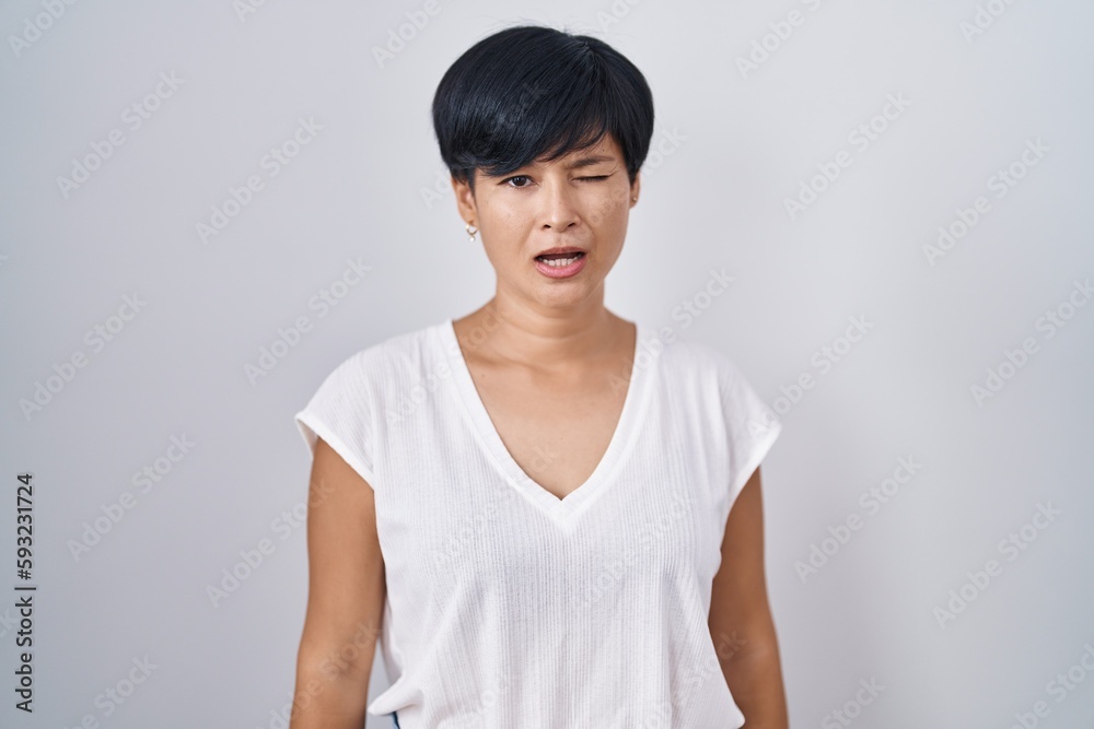 Young asian woman with short hair standing over isolated background winking looking at the camera with sexy expression, cheerful and happy face.